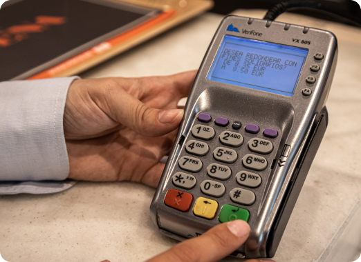 Primer plano de un datáfono de pago con tarjeta con la mano de un cliente, ilustrando el redondeo solidario en caja